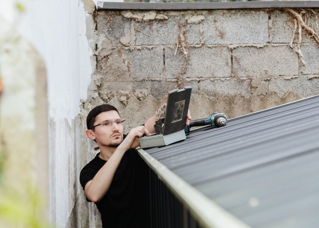 How to Spot Hidden Roof Damage Before It Leads to Expensive Repairs - Vanhook Roofing and Exteriors one young worker installs roof metal shed with drill | Vanhook Roofing and Exteriors
